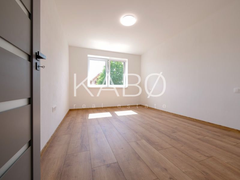 Ein Zimmer in einem Einfamilienhaus mit weißen Wänden und einem Boden in Holzoptik.