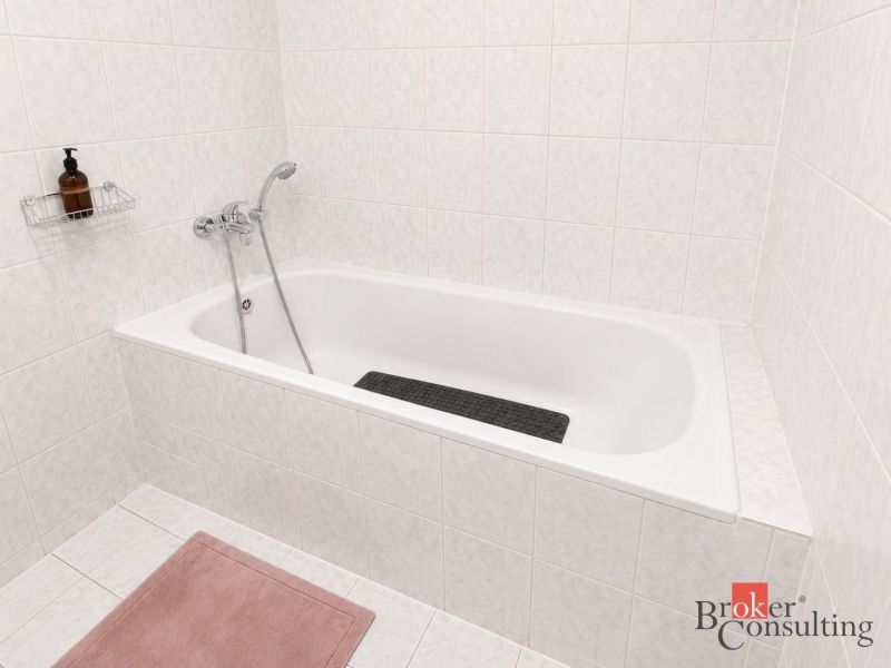 Badezimmer mit einer mit weißen Fliesen verkleideten Badewanne in einer 2-Zimmer-Wohnung.
