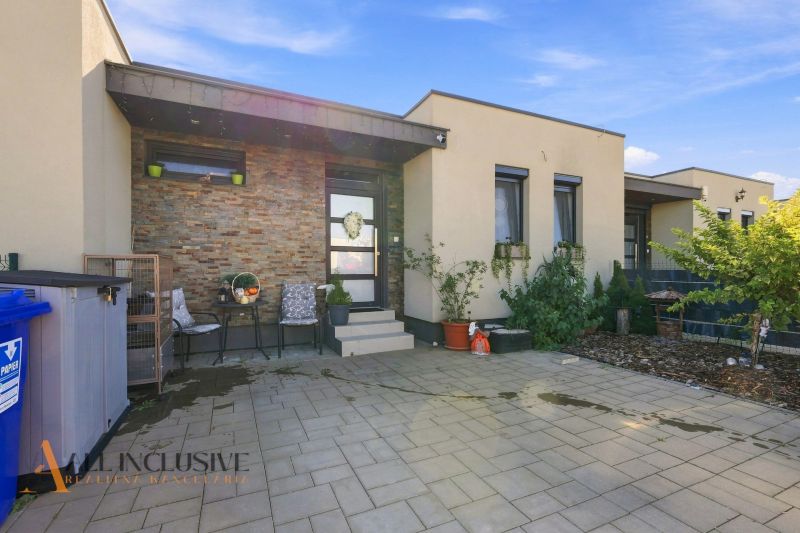 Ein Einfamilienhaus in Oľdza mit einer Terrasse, Blumen und einer bequemen Sitzgelegenheit vor dem Eingang.