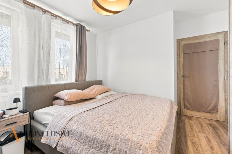 Ein Schlafzimmer in einem Einfamilienhaus mit Holzboden, grauem Bett und Vorhängen.