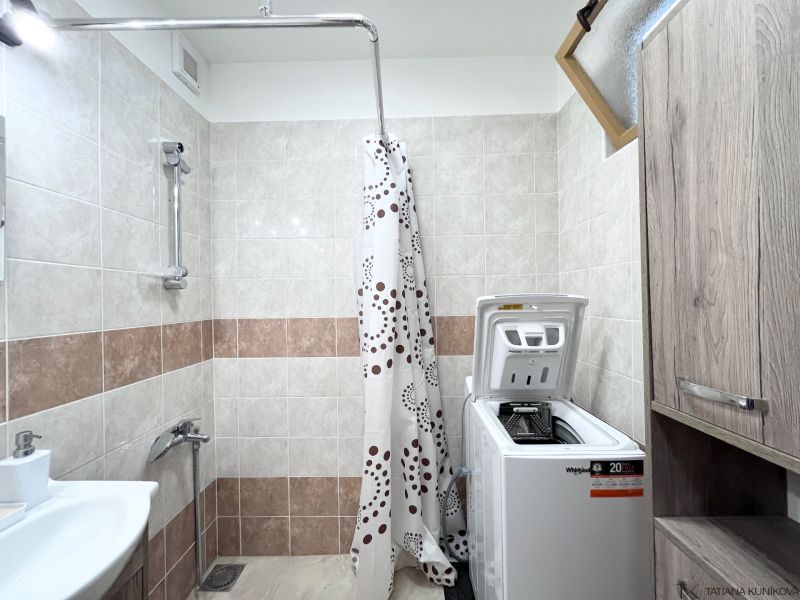 Badezimmer in einer 3-Zimmer-Wohnung mit Waschmaschine, Waschbecken und Duschkabine mit Vorhang.