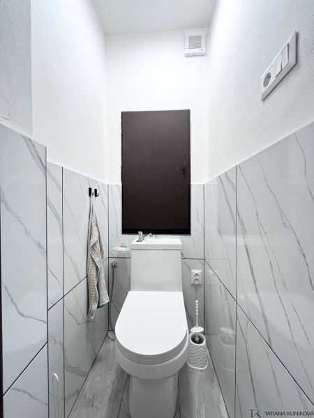 WC in einer 3-Zimmer-Wohnung mit Marmorverkleidung und weißer Sanitärausstattung.