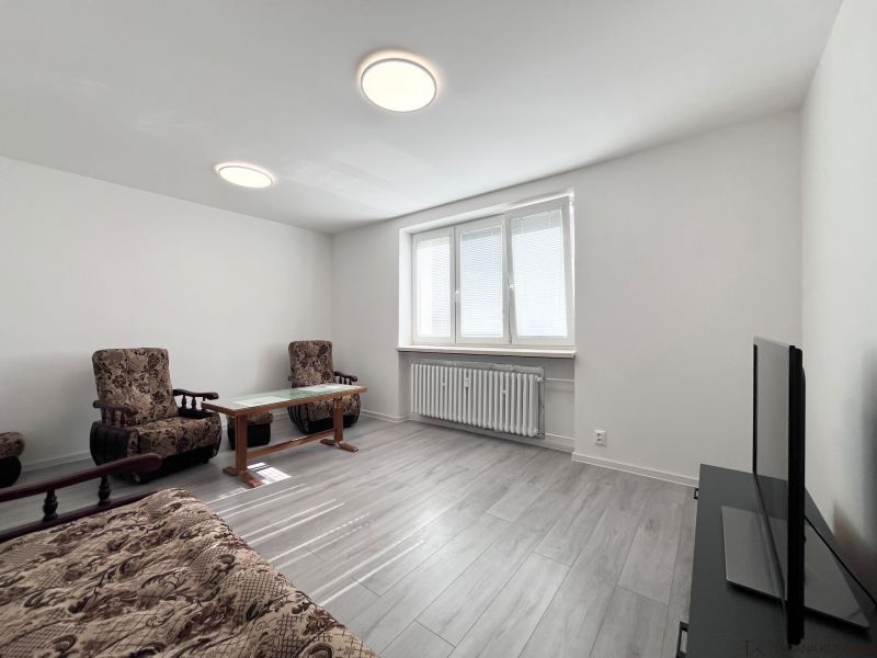 Wohnzimmer in einer 3-Zimmer-Wohnung mit Möbeln, Fernseher und Bodenbelag in Holzoptik.
