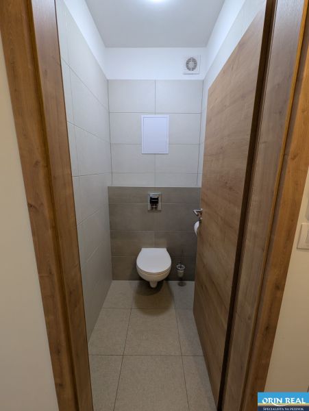 Toilette in einer 2-Zimmer-Wohnung mit Keramikfliesen und einem Boden in Holzoptik.