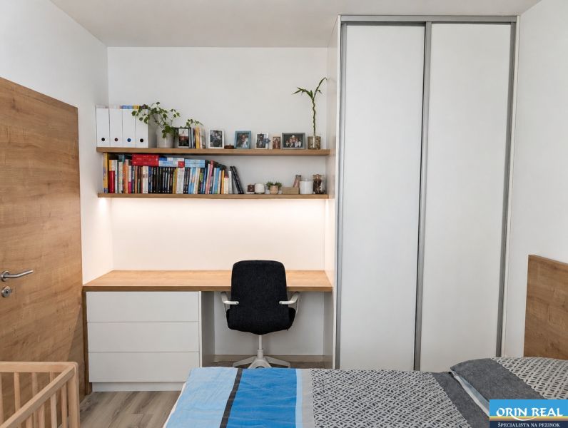 Schlafzimmer in einer 2-Zimmer-Wohnung mit Arbeitsecke, Büchern und Boden in Holzoptik.