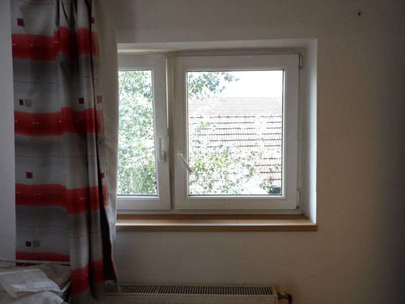 Ein Fenster mit Vorhang und Blick auf das Dach in einer 2-Zimmer-Wohnung.