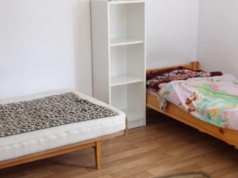 Zwei Betten, ein Regal und ein Boden mit Holzdekor in einer 2-Zimmer-Wohnung.