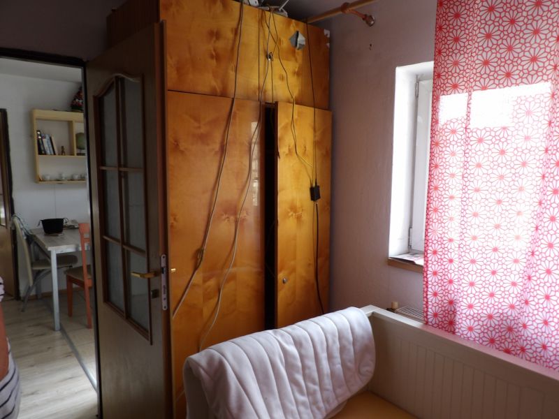 Ein Zimmer in einer Zweizimmerwohnung mit offenen Türen, einem Schrank und einem Vorhang mit rotem Muster.