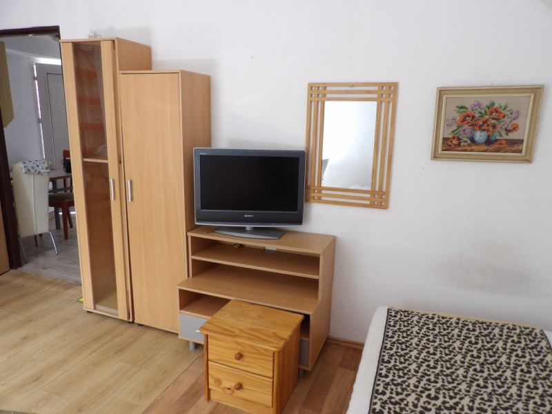 Ein Fernseher auf einem niedrigen Schrank, ein Schrank und ein Spiegel in einer 2-Zimmer-Wohnung mit einem Boden in Holzoptik.