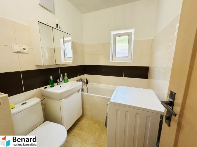 Badezimmer im Einfamilienhaus mit Badewanne, Waschmaschine und Waschbecken, helle Fliesen.
