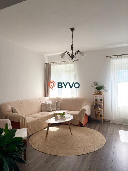 Wohnzimmer mit Holzboden, beigem Sofa und rundem Teppich.