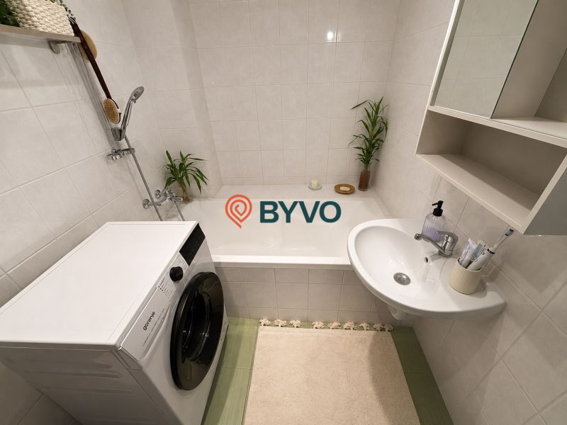 Badezimmer in einer 2-Zimmer-Wohnung mit Badewanne, Waschbecken und Waschmaschine. Neutrale Farbtöne.