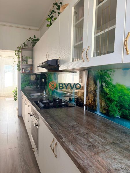 Küche in einer 2-Zimmer-Wohnung mit einem Boden in Holzoptik und einem Waldmotiv an der Wand.