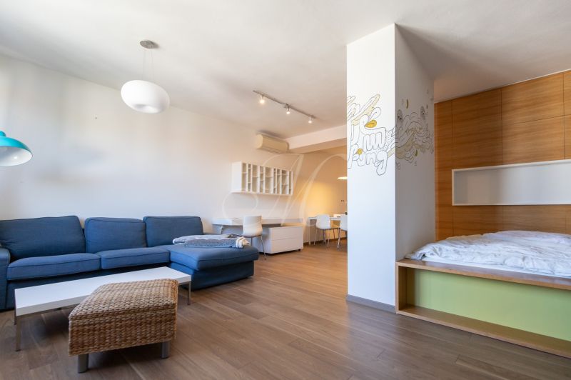 Wohnbereich in einer Einzimmerwohnung mit einem blauen Sofa und einem Boden in Holzoptik.