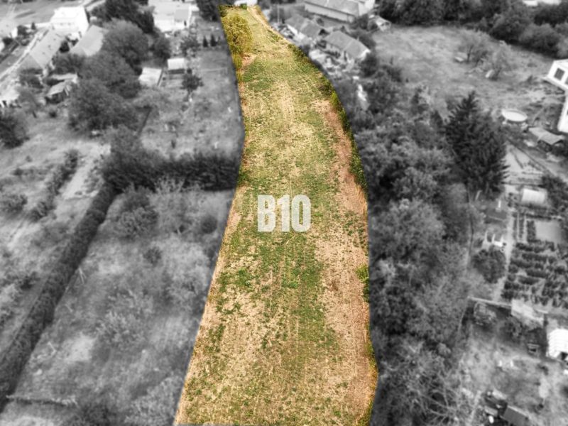 Grundstücke - Wohnen Kolíňany: Langes Grundstück mit grünem Gras, gesäumt von Bäumen und Gebäuden.