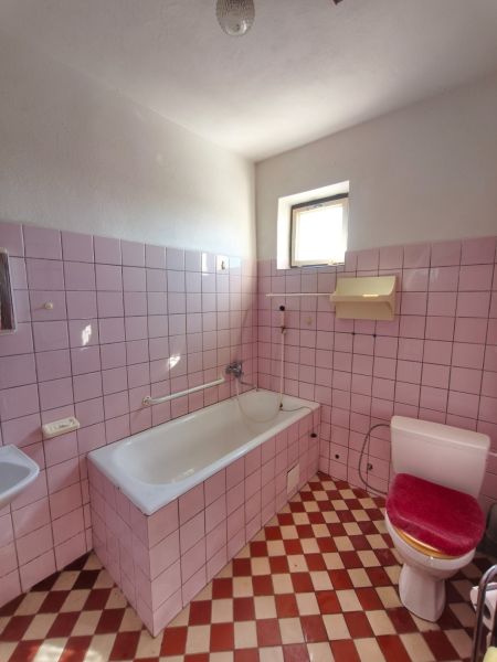 Ein Badezimmer mit rosa Fliesen und einer weißen Badewanne in einem Einfamilienhaus.