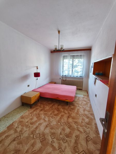 Schlafzimmer im Einfamilienhaus mit Bett, Teppich und Fenster mit weißem Vorhang.
