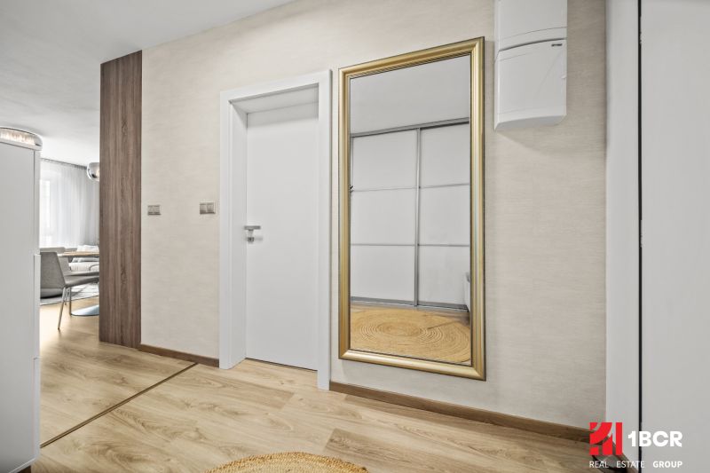 In einer 2-Zimmer-Wohnung befindet sich ein Spiegel mit goldenem Rahmen und ein Boden mit Holzdekor.