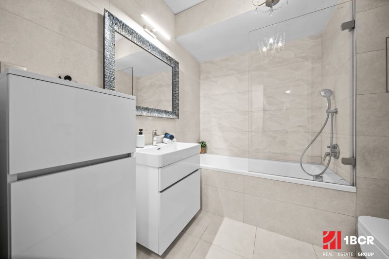 Badezimmer in einer 2-Zimmer-Wohnung mit Dusche und Badewanne, helle Fliesen.