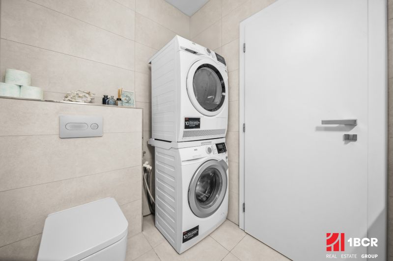 Waschmaschine mit Trockner im Badezimmer einer 2-Zimmer-Wohnung, helle Fliesen und Toilette.