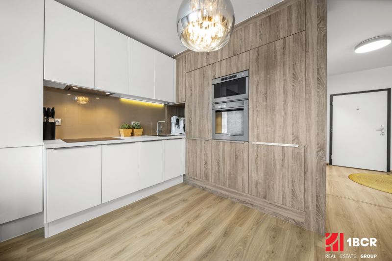 Küche in einer 2-Zimmer-Wohnung, weiße Schränke, Boden mit Holzdekor, eingebaute Geräte.