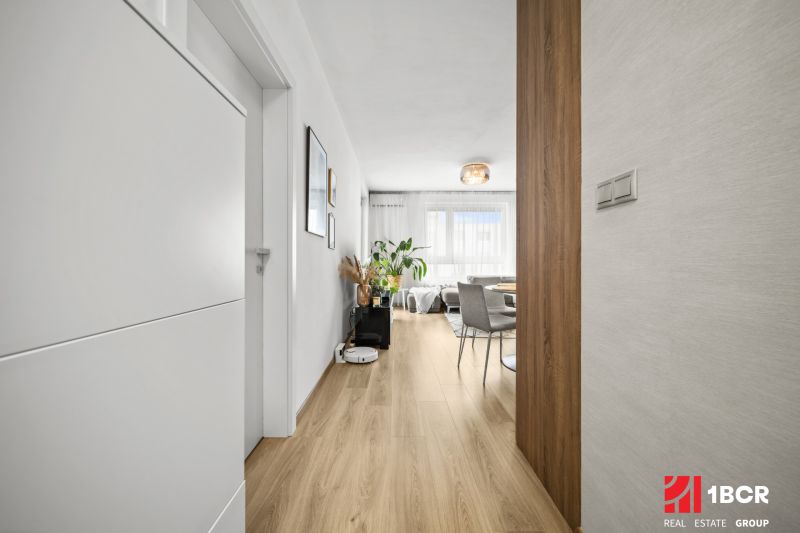 Ein Flur mit einem Holzboden, der in das Wohnzimmer einer Zweizimmerwohnung führt.