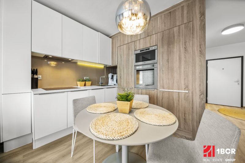 Küche in einer 2-Zimmer-Wohnung mit Holzboden, Tisch und eingebauten Geräten.