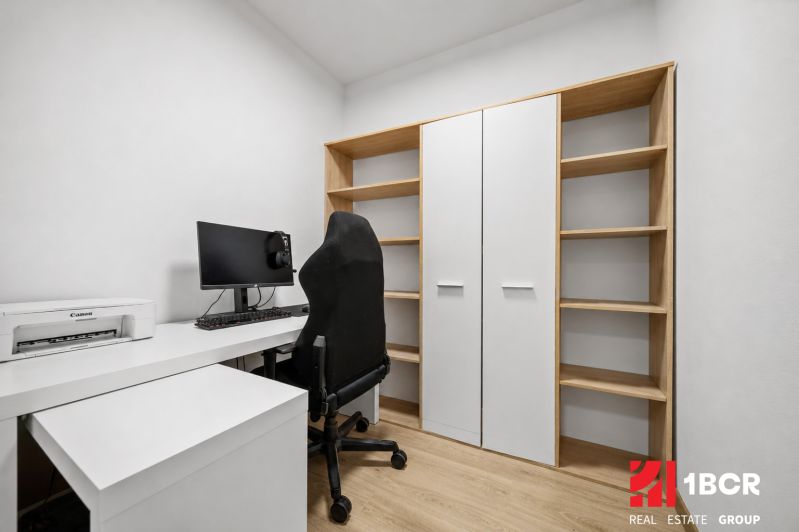 Ein Arbeitsbereich mit Computer, Drucker und Regalen in einer 2-Zimmer-Wohnung mit einem Holzboden.