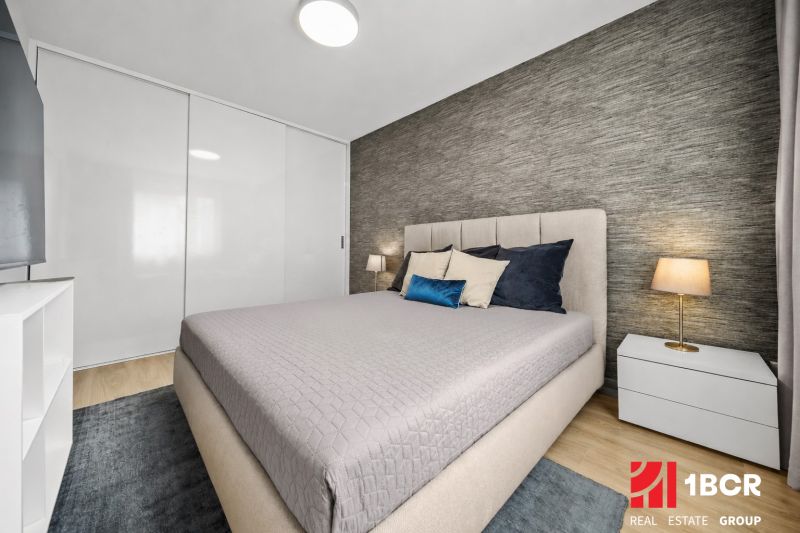 Schlafzimmer in einer 2-Zimmer-Wohnung mit Bett, Nachttischen und Boden mit Holzdekor.