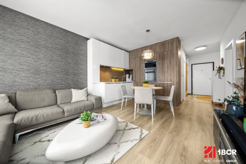 Wohnzimmer in einer Zweizimmerwohnung mit Sofa und Küchenzeile, Holzboden.