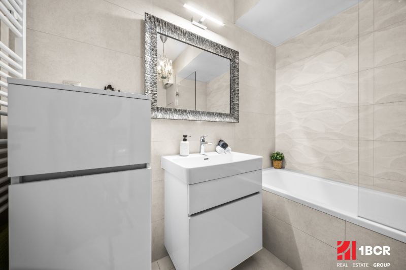 Badezimmer mit Spiegel, Waschbecken und Badewanne in einer 2-Zimmer-Wohnung; sauberes und helles Design.