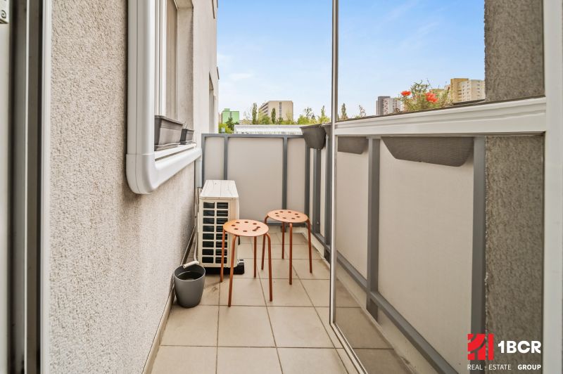 Balkon mit zwei orangefarbenen Stühlen in einer Zweizimmerwohnung mit Blick auf die Stadt.