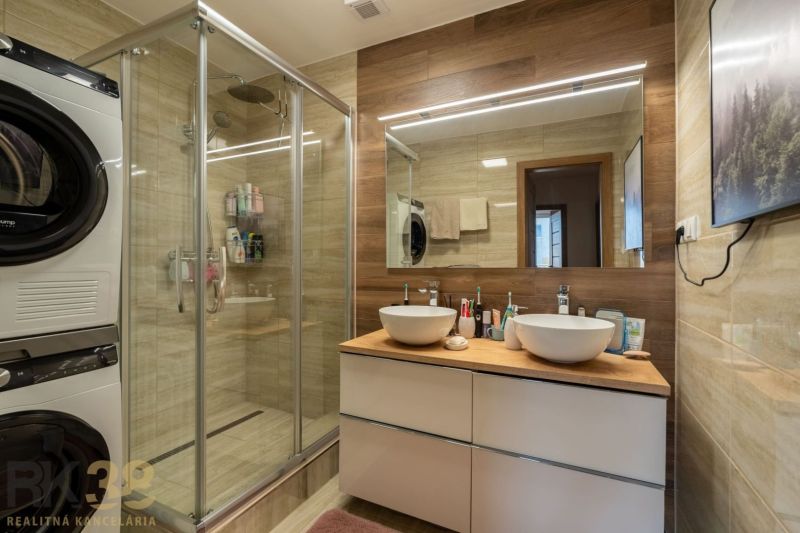 Badezimmer in einer 3-Zimmer-Wohnung mit Doppelwaschbecken, Duschkabine und Waschmaschine.