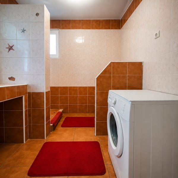 Badezimmer in einem Einfamilienhaus mit Dusche und Waschmaschine, Fliesen in Brauntönen.