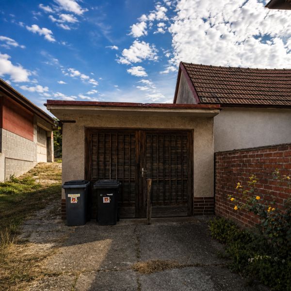 Einfamilienhaus mit Garage in Šalgočka, mit zwei Mülleimern und einer Ziegelmauer.