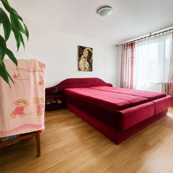Schlafzimmer im Einfamilienhaus mit rotem Bett und Boden in Holzoptik.