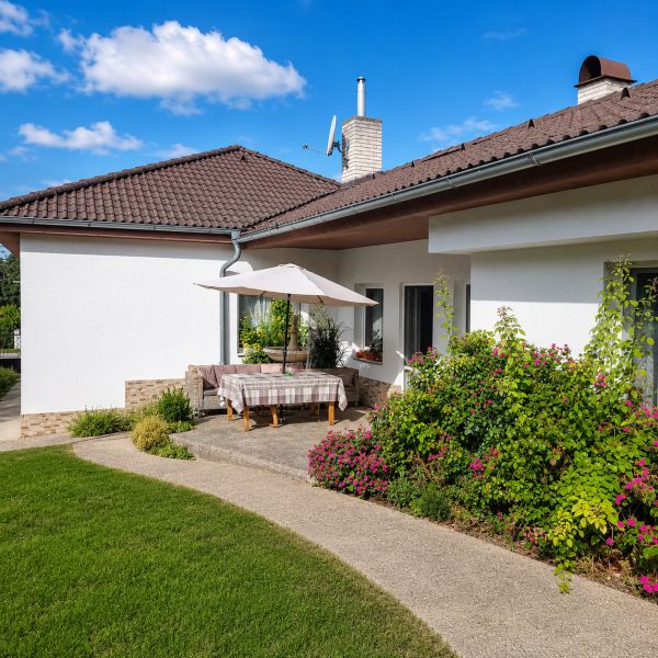 Ein Einfamilienhaus in Šalgočka mit Terrasse, Garten und Sonnenschirm auf einem Rasenstück.