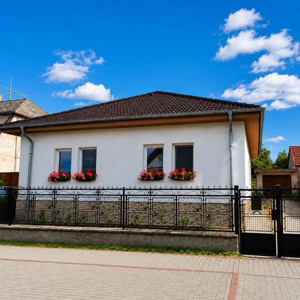 Ein Einfamilienhaus in Šalgočka mit weißer Fassade, Fensterblumen und einem Walmdach.