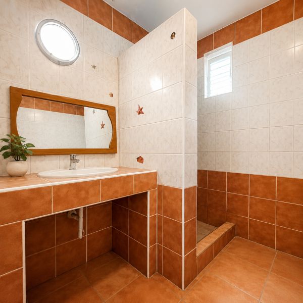 Ein Badezimmer in einem Einfamilienhaus mit Keramikfliesen und einem Holzspiegel.