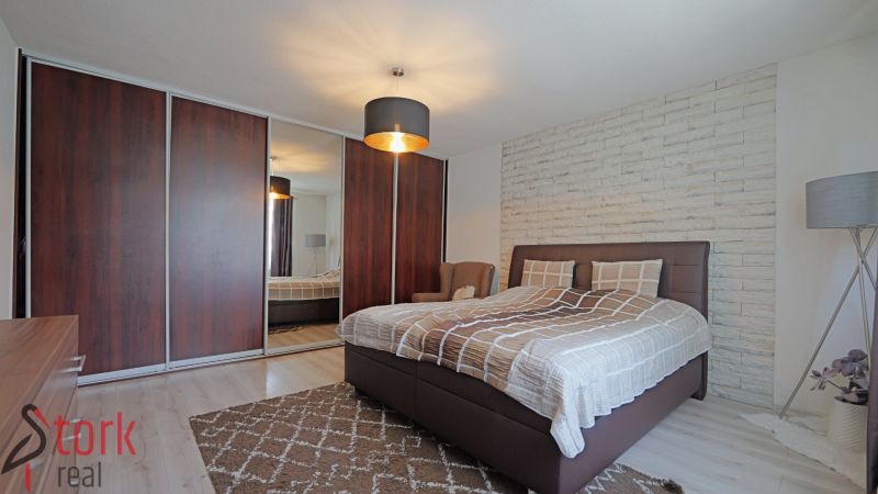 Schlafzimmer in einem Einfamilienhaus mit Bett, Holzschränken und weißer Steinwand.