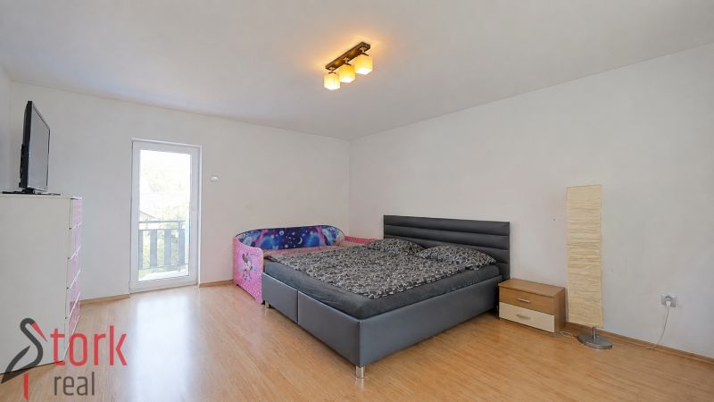 Ein Schlafzimmer in einem Einfamilienhaus mit einem Bett, einem Kinderbett und einem Boden mit Holzdekor.
