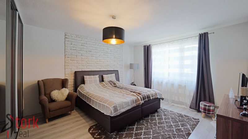 Schlafzimmer mit einem bequemen Bett und einem Sessel; Boden mit Holzdekor in einem Einfamilienhaus.