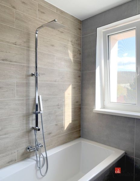 Badezimmer mit Badewanne und Dusche, Fliesen mit Holzdekor, großes Fenster, Einzimmerwohnung.