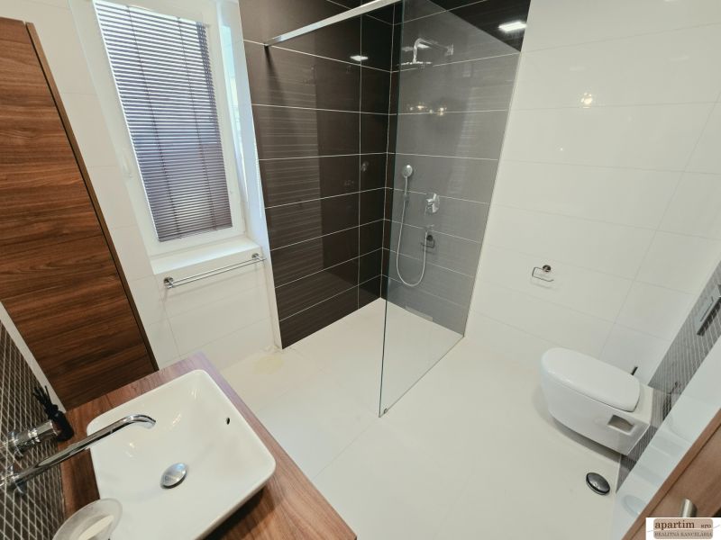 Badezimmer in einer 4-Zimmer-Wohnung mit Waschbecken, Dusche und dunklen Fliesen.