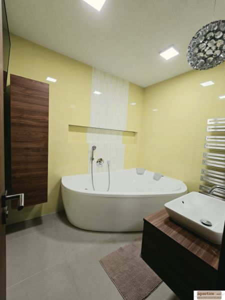 Ein Badezimmer mit gelben Fliesen, einer Eckbadewanne und einem Holzdekor am Schrank in einer 4-Zimmer-Wohnung.