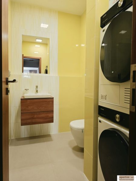 Badezimmer in einer 4-Zimmer-Wohnung, hellgelbe Fliesen, Waschbecken, Toilette, Waschmaschine und Trockner.
