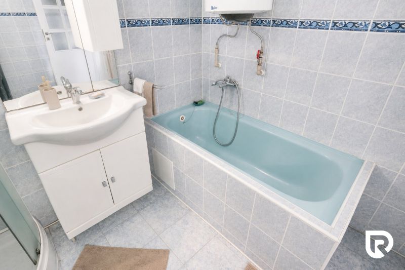 Badezimmer mit weißem Waschtischunterschrank und blauer Badewanne in einem Einfamilienhaus.