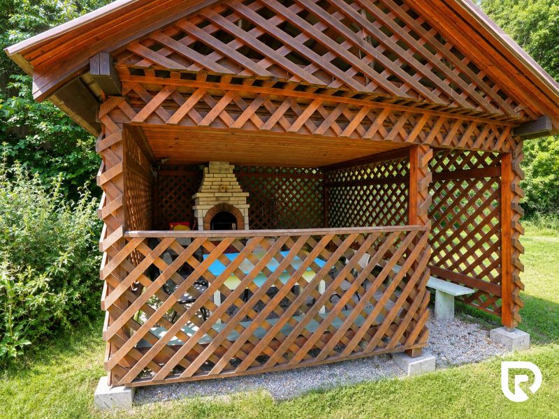 Pavillon mit Holzgittern und Außengrill im Garten bei einem Einfamilienhaus.