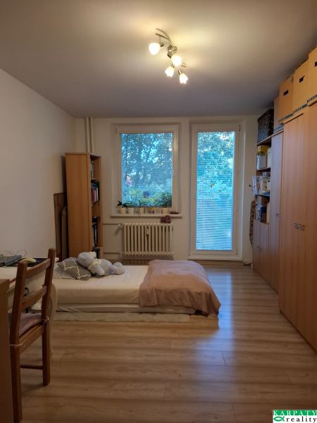 Ein Zimmer in einer 3-Zimmer-Wohnung mit einem Bett, Regalen und einem Boden in Holzoptik.