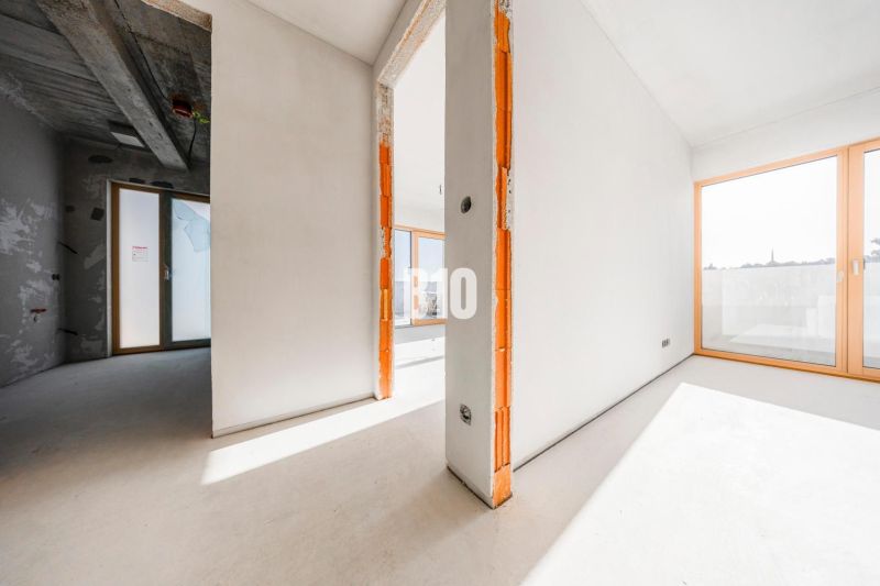 Geräumiges Interieur einer unvollendeten 3-Zimmer-Wohnung mit großen Fenstern und Betondecke.